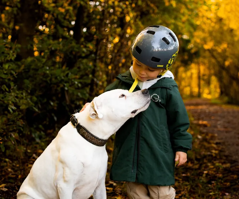 Ein kleiner Junge mit Helm und ein weisser Hund schauen sich liebevoll an